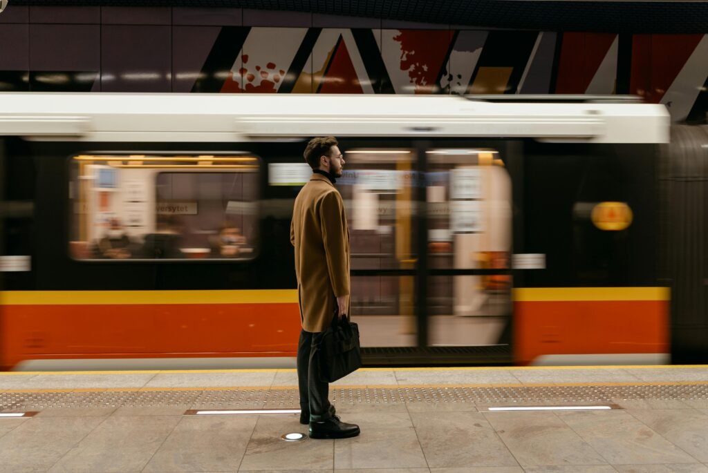 A man in a coat holding a briefcase stands at a train station platform as a train passes by.